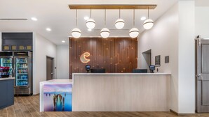 Un área de recepción con un mostrador de madera, una pantalla digital y una máquina expendedora.
