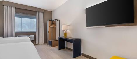 Habitación de hotel con cama, escritorio, silla, televisión y ventana con cortinas.
