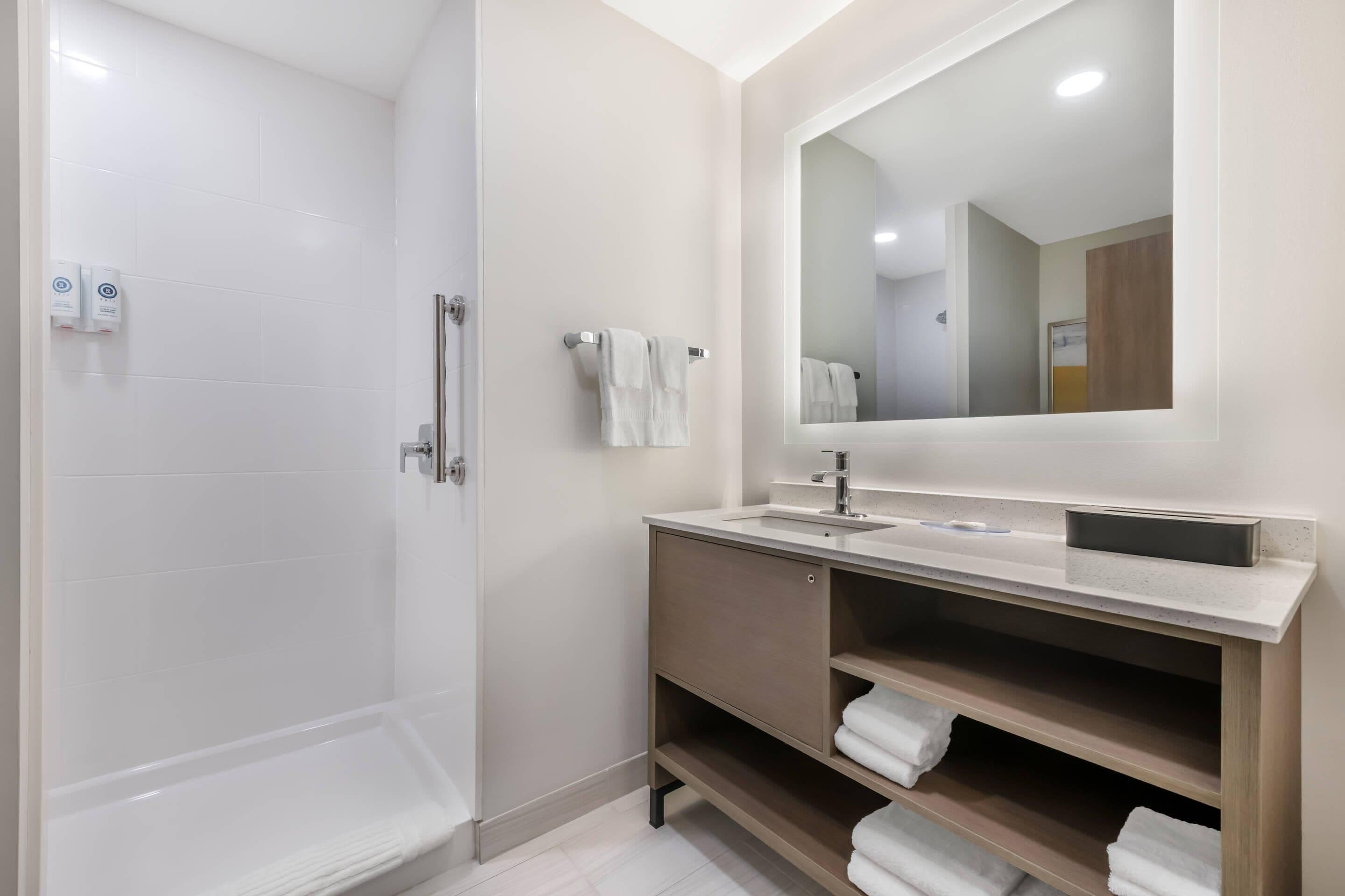 A modern bathroom with a walk-in shower, a sink with a mirror, and shelves for towels.