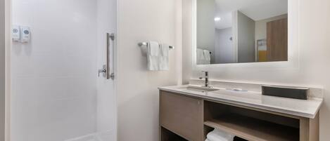 A modern bathroom with a walk-in shower, a sink with a mirror, and shelves for towels.