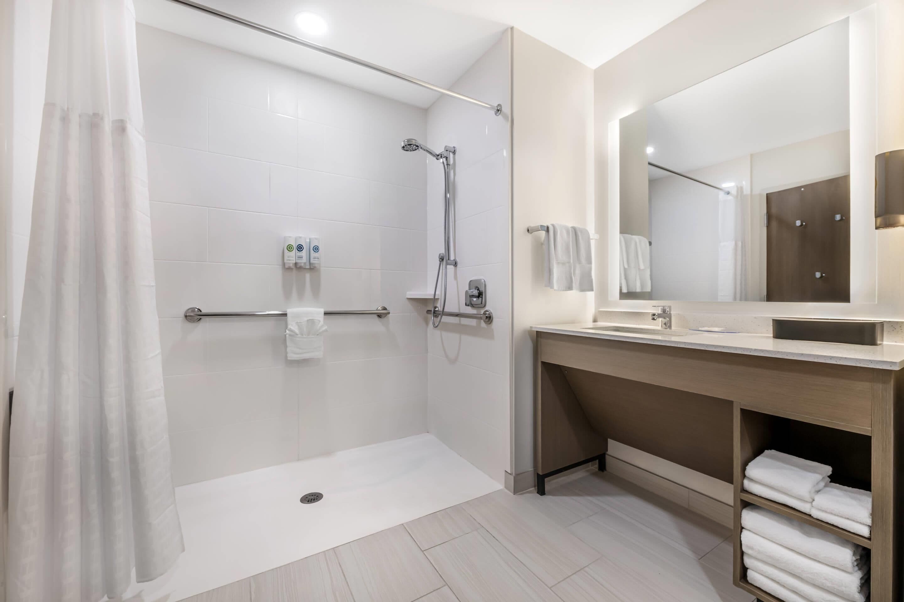 A modern bathroom with a walk-in shower, a vanity with a mirror, and a shelf with towels.