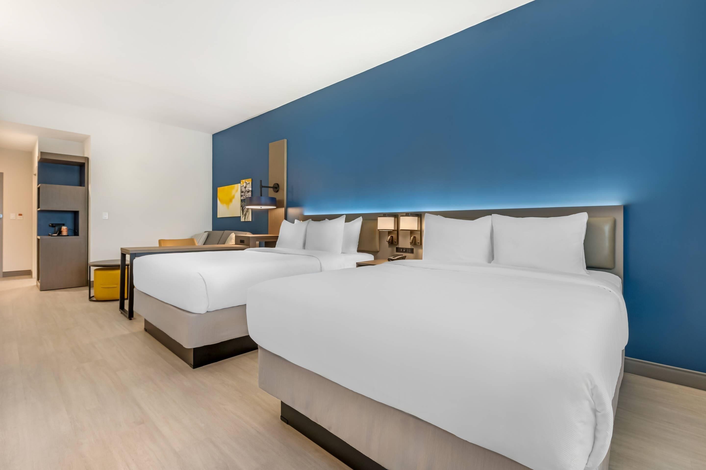 A hotel room with two beds, a desk, a chair, a small table, and a wardrobe.