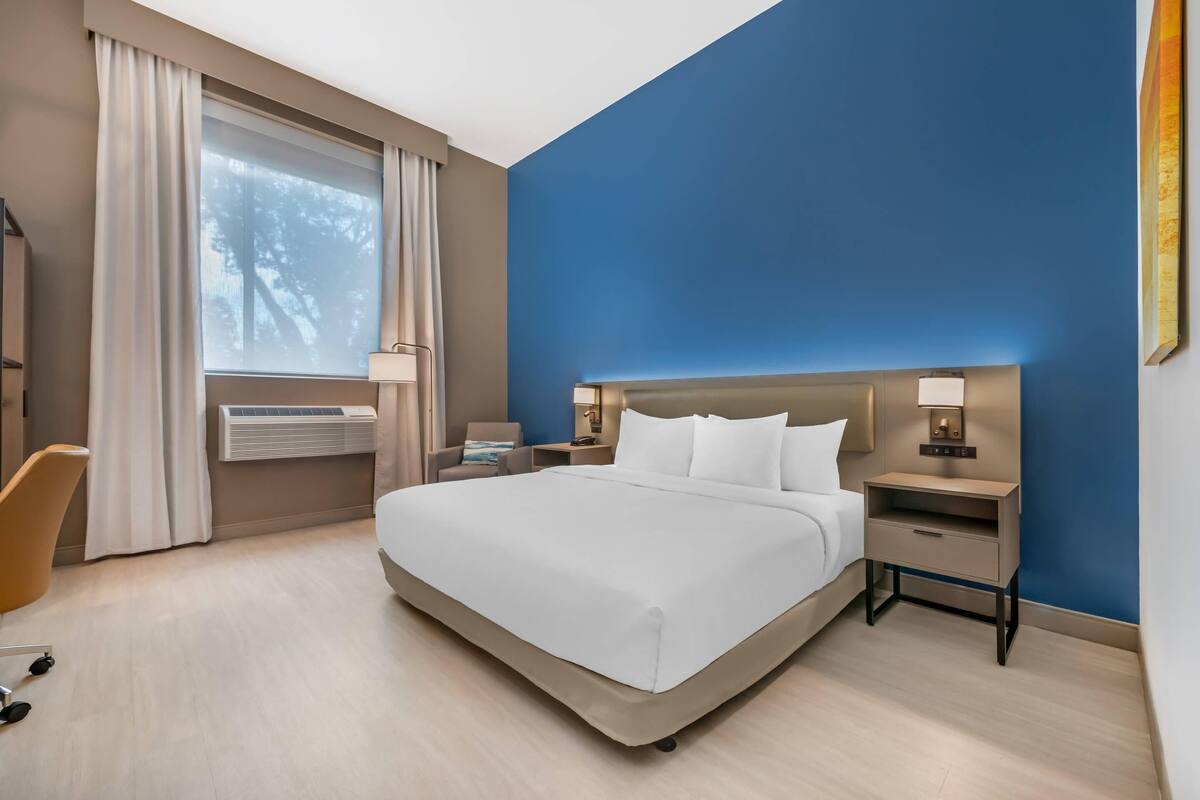 Ett modernt hotellrum med en stor säng, sängbord med lampor, ett skrivbord och en stol.