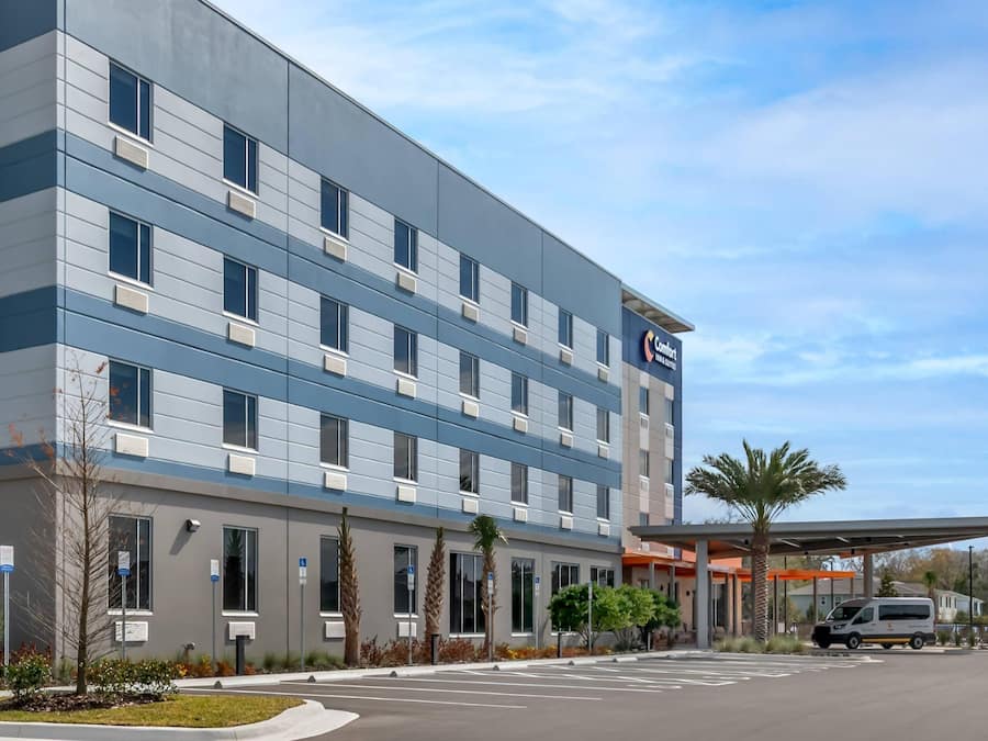 A modern hotel building with a flat facade, multiple windows, and a parking lot.