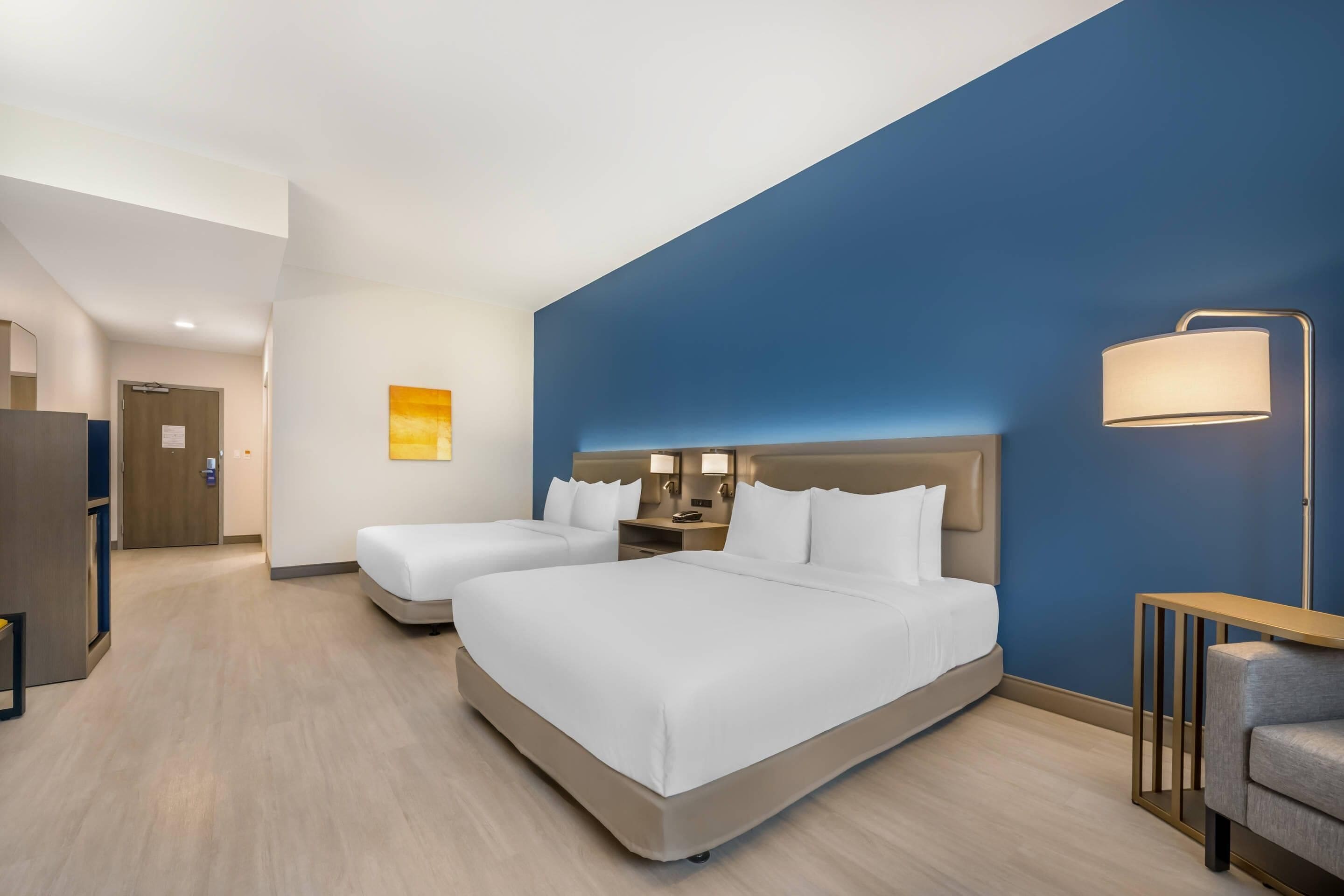 Habitación de hotel con dos camas, un escritorio, una silla y una mesita de noche.