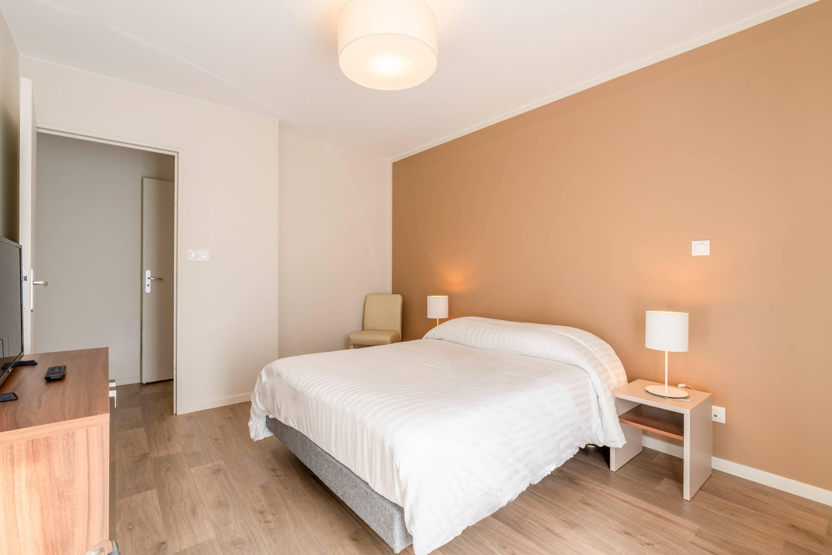 A bedroom with a bed, bedside tables, a chair, and a desk with a lamp.