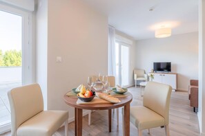 A modern hotel room with a dining area, a television, and a balcony with a view of trees. - Quality Aparthotel Grenoble Sud (Echirolles)