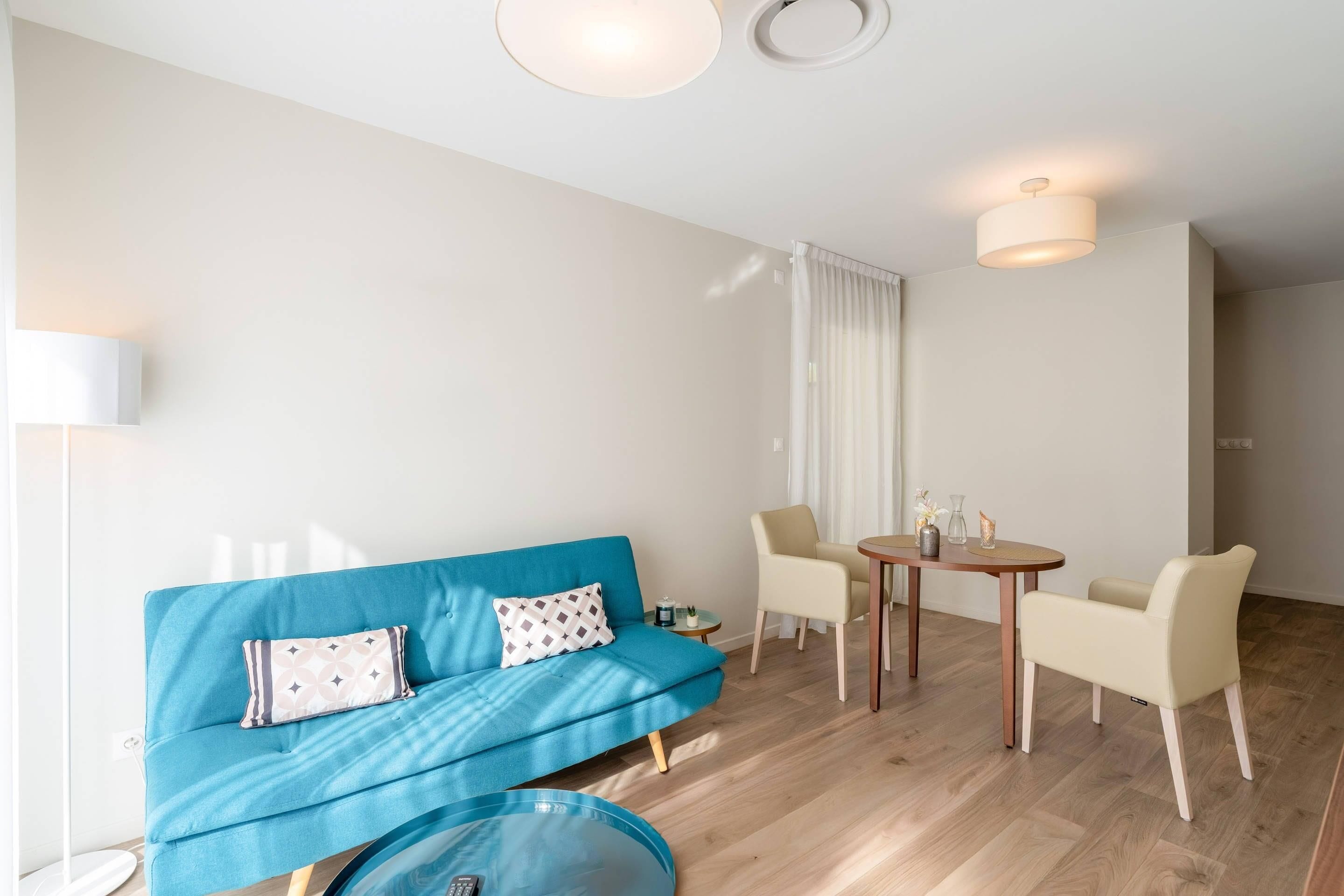 Una sala de estar moderna con un sofá azul, dos sillones, una mesita y una mesa redonda de centro.