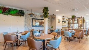 Un restaurante moderno con mesas redondas y sillas azules, un adorno de pared verde y una barra de madera.
