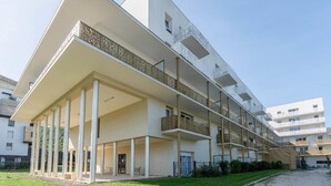 Un edificio moderno de varios pisos con techo plano, balcones y un área exterior cubierta con columnas.