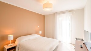 Una habitación de hotel con cama, mesita de noche, lámpara y un escritorio con silla.