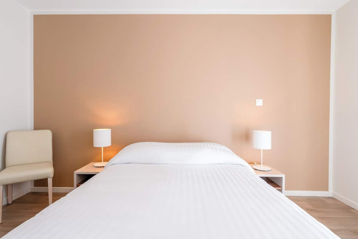 Un dormitorio con cama, dos lámparas de noche, una silla y una mesita de noche.
