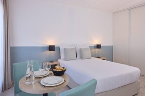 A hotel room with a bed, a round dining table with chairs, a basket of bread, and two bedside lamps. - Quality Aparthotel Marseille Centre Lodi (Marseille)