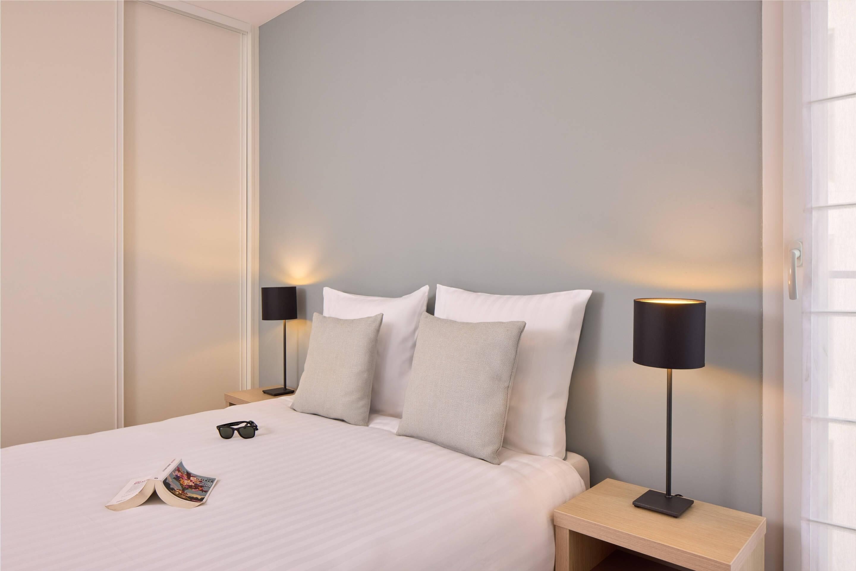 A neatly made bed with pillows, a bedside lamp, and a magazine on the bed.