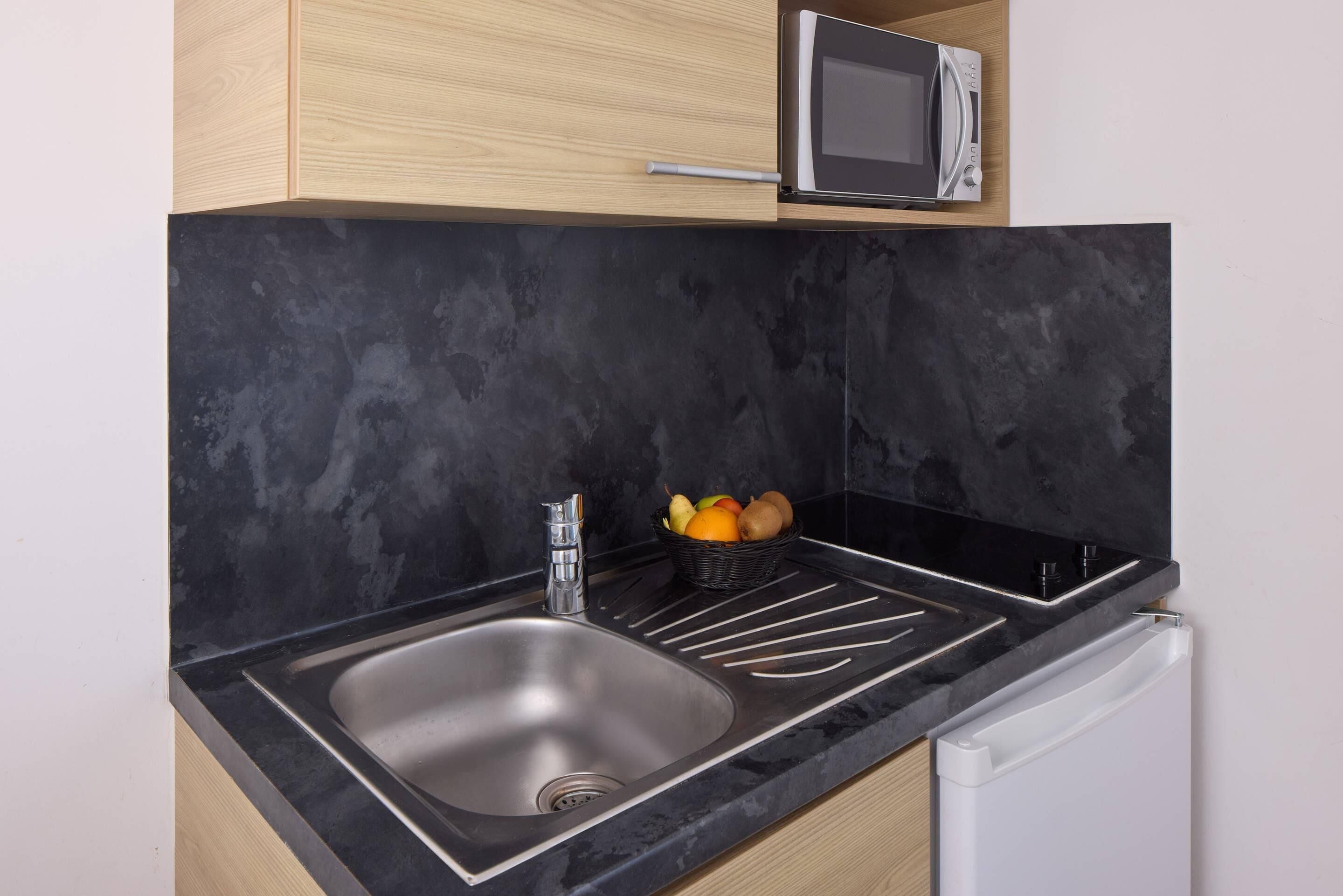 Una cocina con encimera negra, pileta de acero inoxidable y un microondas encima.
