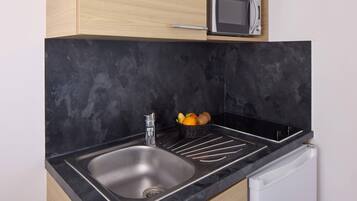 Una cocina con encimera negra, pileta de acero inoxidable y un microondas encima.