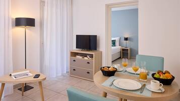 A hotel room with a dining table set for breakfast, a TV, a bedside table, and a bed in the background.