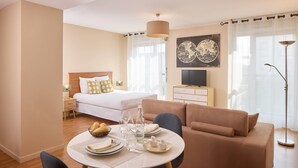 A modern hotel room with a bed, a sofa, a dining area with a table set for two, and a flat-screen TV on a dresser. - Quality Aparthotel Chalon-sur-Saône Gare (Chalon-sur-Saone)