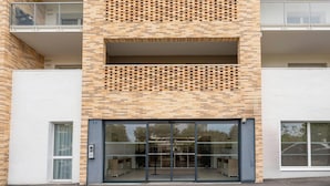 Ein modernes Gebäude mit Ziegelaußenwand, großem Glas Eingang und einem Balkon im oberen Geschoss.