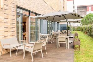 Une terrasse extérieure dotée d’un plancher en bois, de mobilier blanc et de grands parasols offrant de l’ombre.