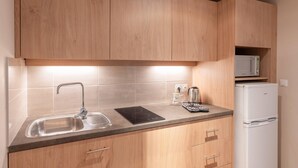 A kitchen with wooden cabinets, a stainless steel sink, a black induction cooktop, a kettle, and a white refrigerator. - Quality Aparthotel Toulouse Ponts Jumeaux (Toulouse)