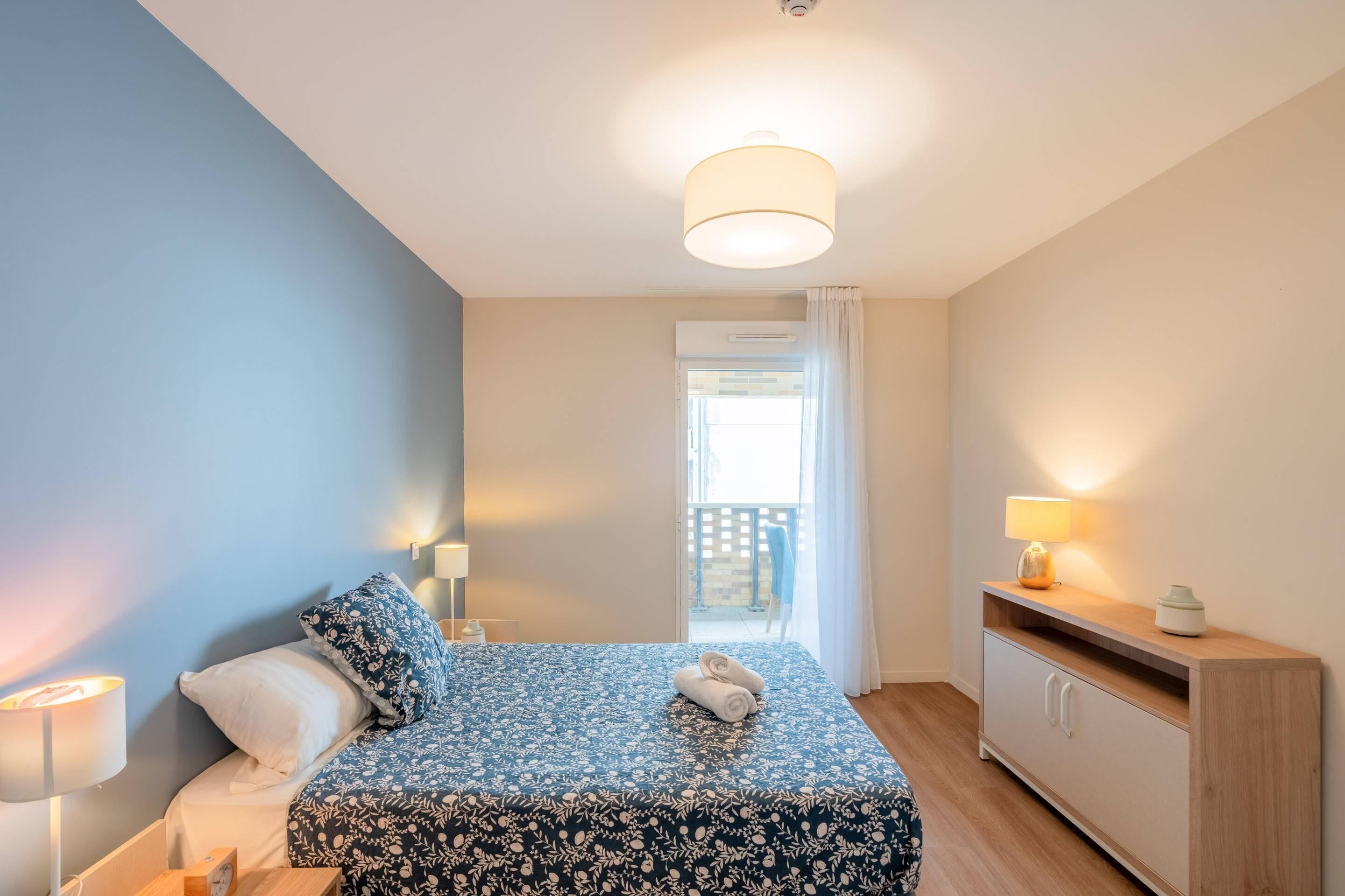 Une chambre à coucher avec un lit, des lampes de chevet, une table de chevet, une commode et une vue sur le balcon.