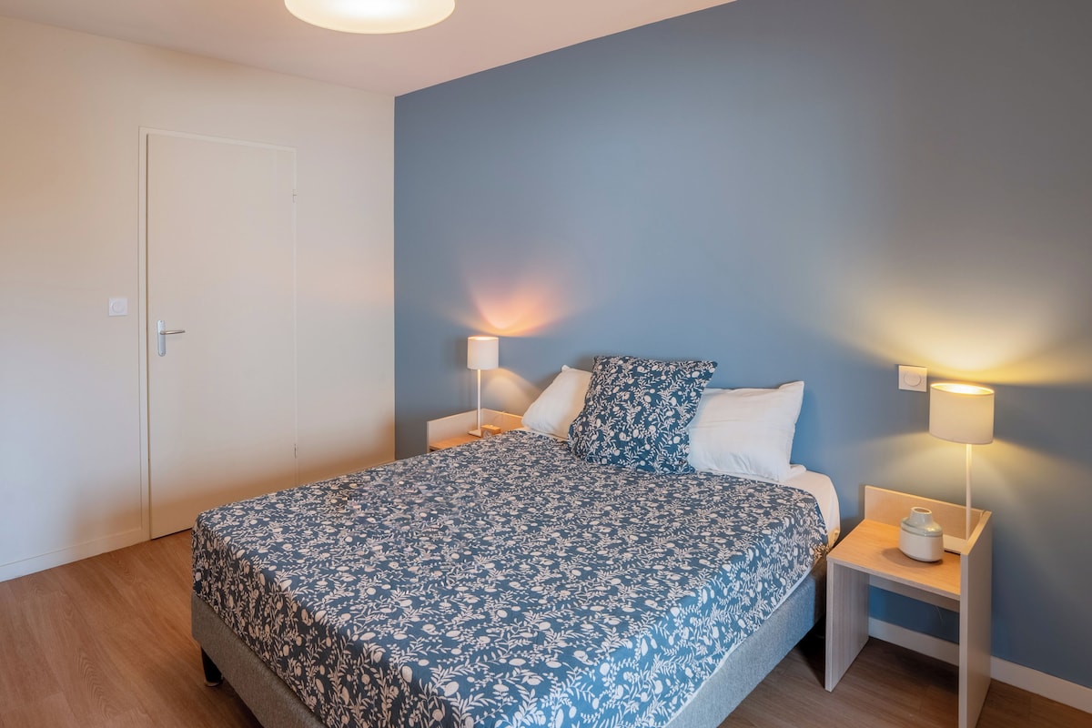 A bedroom with a bed, two bedside tables, a nightstand, a door, and a wall-mounted light fixture.
