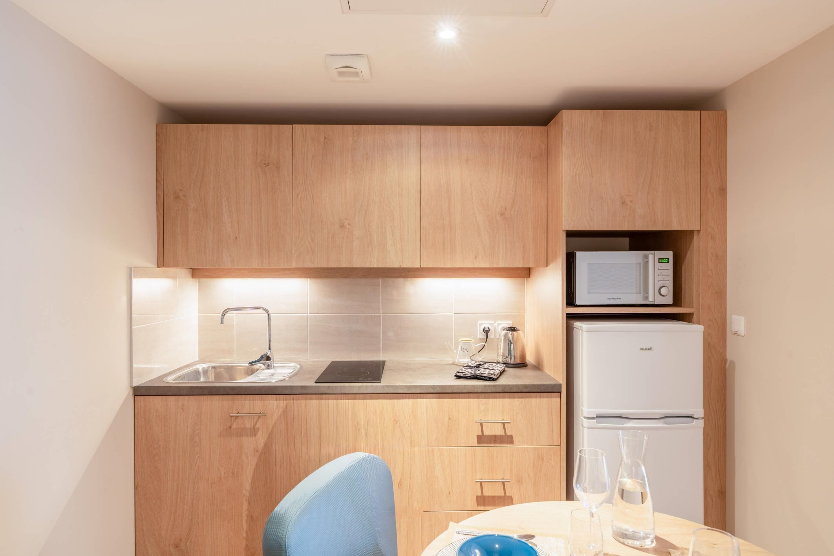 Une cuisine compacte dotée de meubles en bois, d’un four à micro-ondes, d’un réfrigérateur, d’un évier et d’un coin repas avec une chaise et une table.