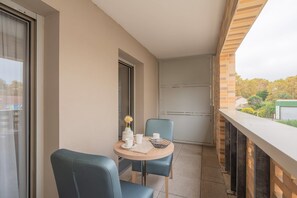Un balcon avec une table dressée pour deux personnes, un vase rempli de fleurs et une vue sur les environs.
