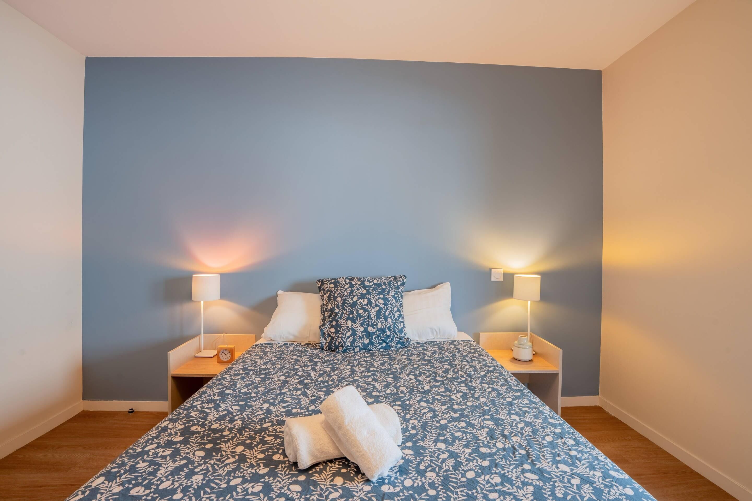 Ein Schlafzimmer mit einem Bett, zwei Nachttischen mit Lampen und einer blauen Wand.