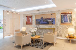 A modern hotel lobby with a seating area, decorative wall art, and a view of the outside. - Quality Aparthotel Toulouse Ponts Jumeaux (Toulouse)