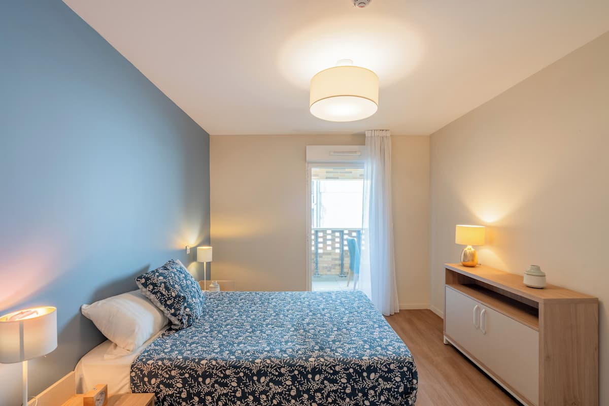 Une chambre à coucher avec un lit, des lampes de chevet, une table de chevet, une commode et une vue sur l’extérieur.