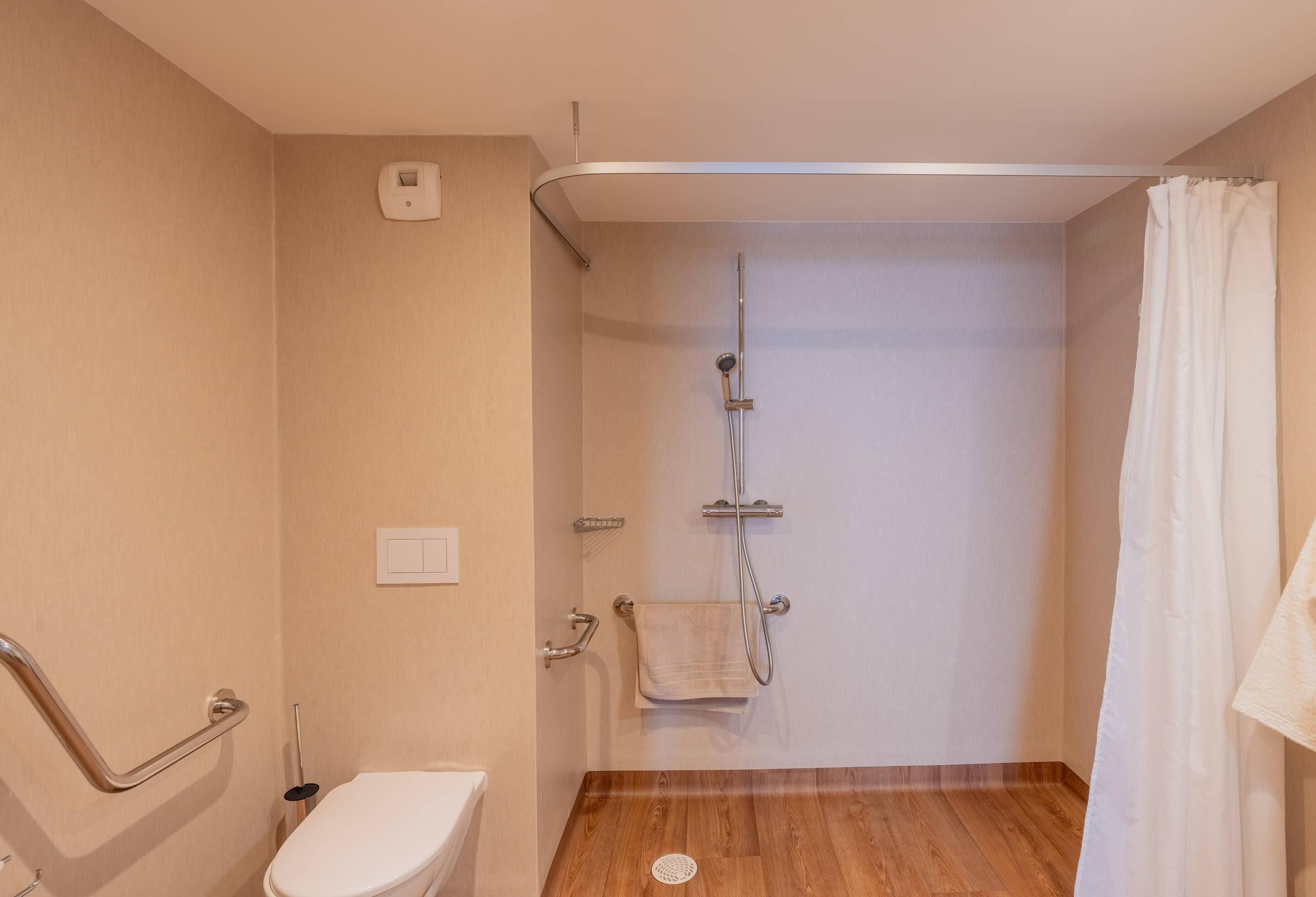 Baño con ducha, inodoro y barra de apoyo.