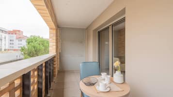 A balcony with a table set for tea, a chair, and a vase with a flower.
