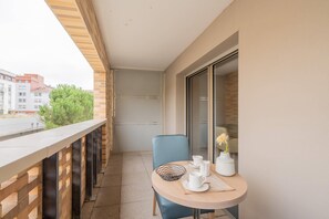 A balcony with a table set for tea, a chair, and a vase with a flower. - Quality Aparthotel Toulouse Ponts Jumeaux (Toulouse)
