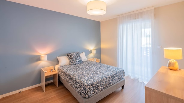 Ein Schlafzimmer mit einem Bett, zwei Nachttischen, einer Lampe und einem Fenster mit Vorhängen.