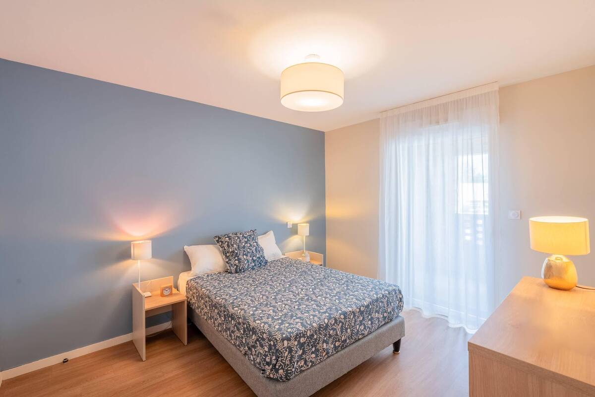 Ein Schlafzimmer mit einem Bett, zwei Nachttischen, einer Lampe und einem Fenster mit Vorhängen.
