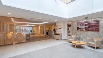 Un hall d’entrée spacieux avec un plafond haut, un comptoir d’accueil, un espace salon et une grande fenêtre laissant entrer la lumière naturelle.