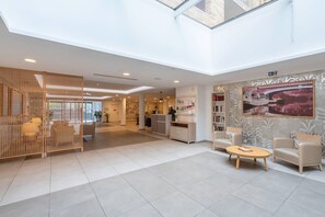 A spacious lobby with a high ceiling, a reception desk, seating area, and a large window providing natural light. - Quality Aparthotel Toulouse Ponts Jumeaux (Toulouse)