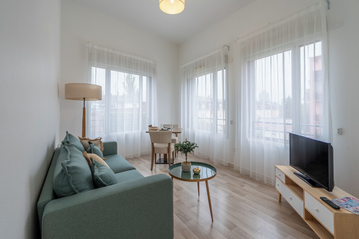 A modern living room with a sofa, a coffee table, a television, and a dining area with a table and chairs.