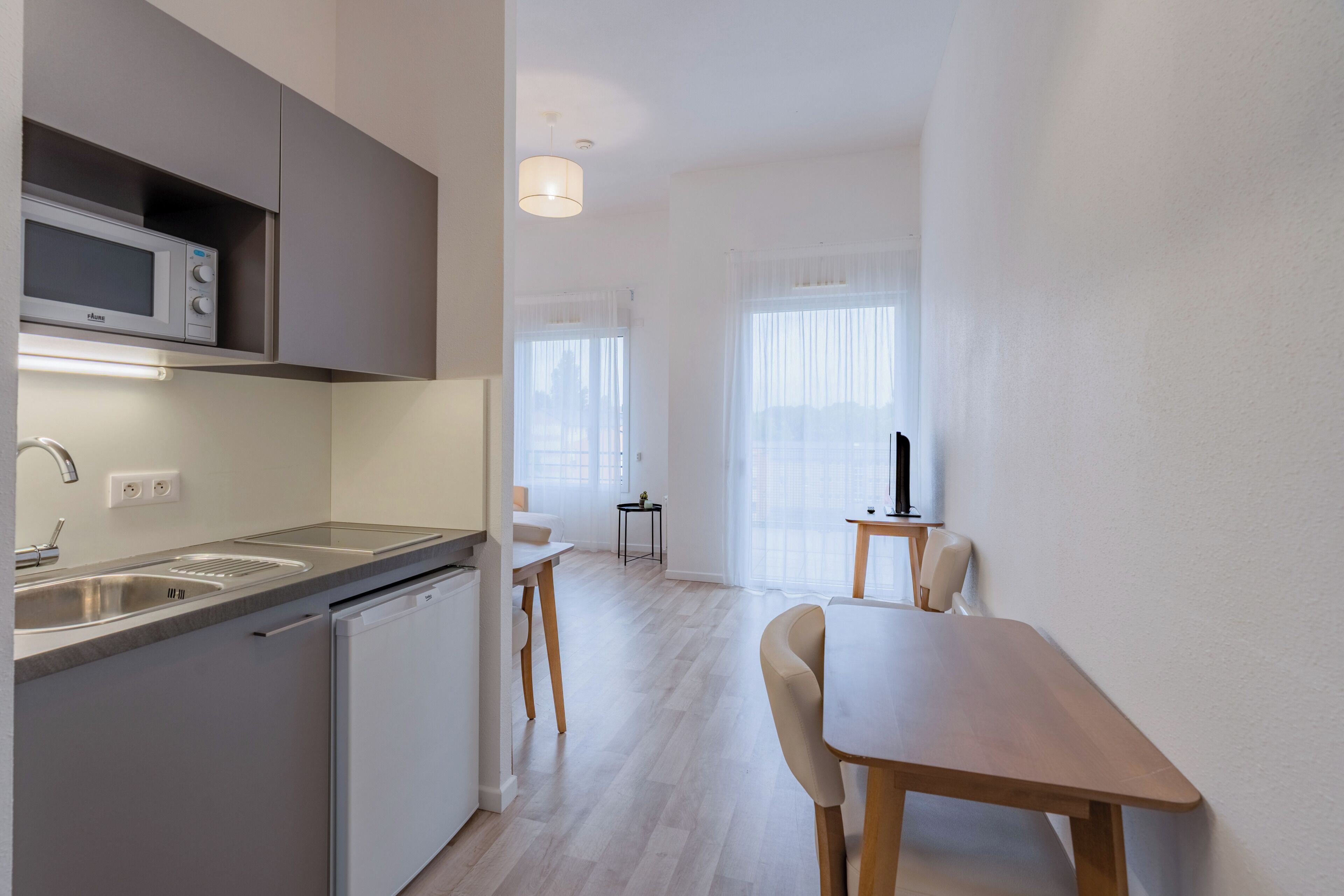Une cuisine moderne équipée d’un four à micro-ondes, d’un évier et d’un lave-vaisselle, un coin repas avec une table et des chaises, et une petite table d’appoint avec une lampe.