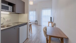 A modern kitchen with a microwave, sink, and dishwasher, a dining area with a table and chairs, and a small side table with a lamp. - Quality Aparthotel Mulhouse (Mulhouse)