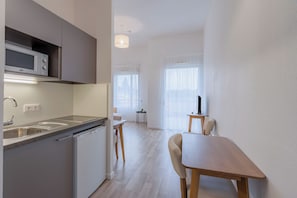A modern kitchen with a microwave, sink, and dishwasher, a dining area with a table and chairs, and a small side table with a lamp. - Quality Aparthotel Mulhouse (Mulhouse)