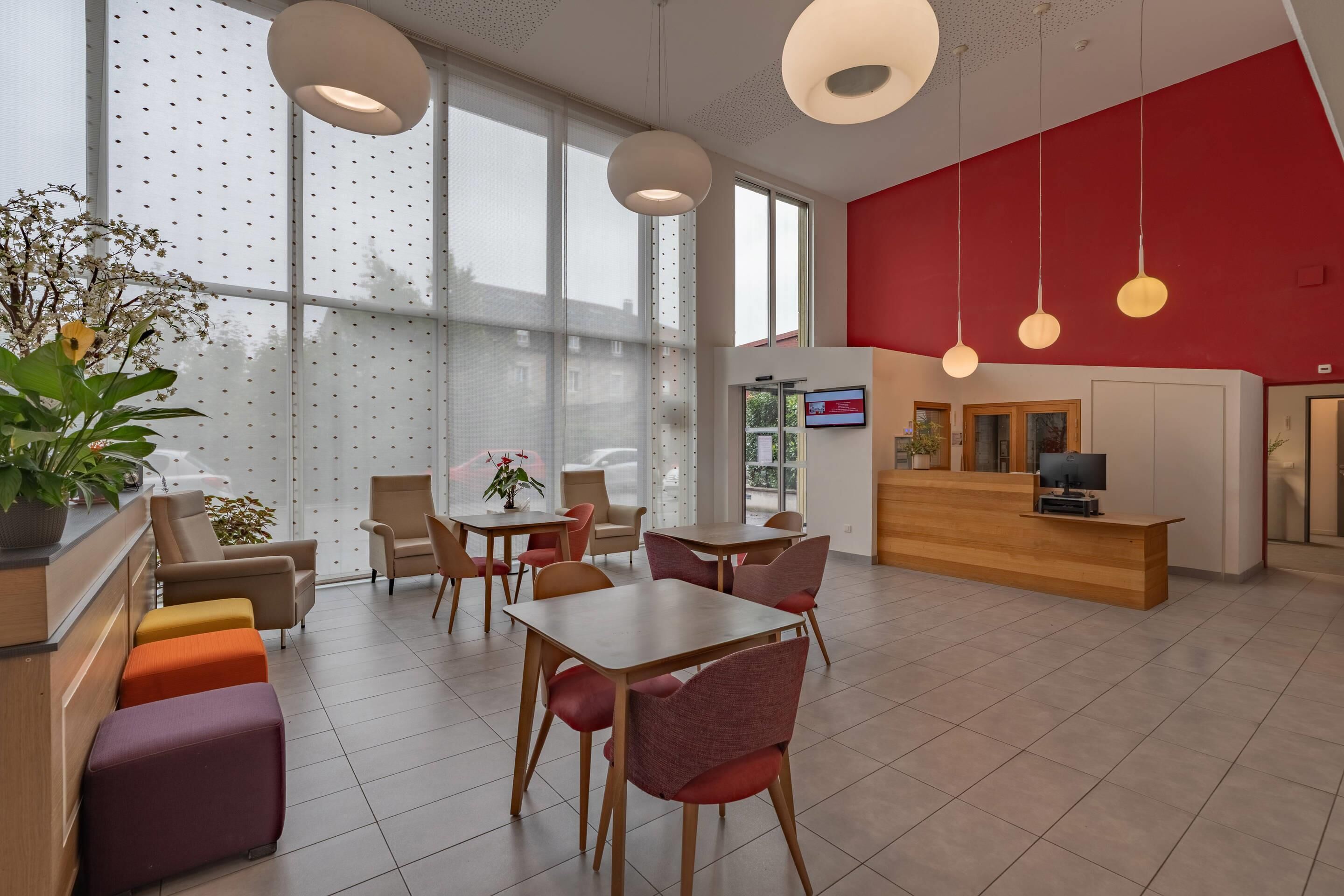 Een moderne hotellobby met een receptiebalie, een zithoek en grote ramen.