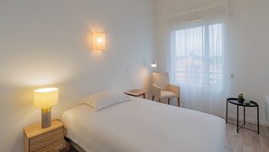 A hotel room with a bed, bedside table, lamp, chair, and a small table with a plant. - Quality Aparthotel Mulhouse (Mulhouse)