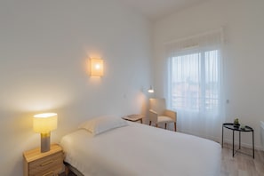 A hotel room with a bed, bedside table, lamp, chair, and a small table with a plant. - Quality Aparthotel Mulhouse (Mulhouse)