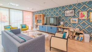 A modern living room with a sofa, armchairs, a coffee table, and a TV. There are bookshelves and a patterned wall. - Quality Aparthotel Villefontaine (Villefontaine)