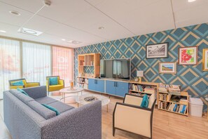 Una sala de estar moderna con sofá, sillones, una mesa de centro y televisor. Se observan estanterías y una pared con diseño.
