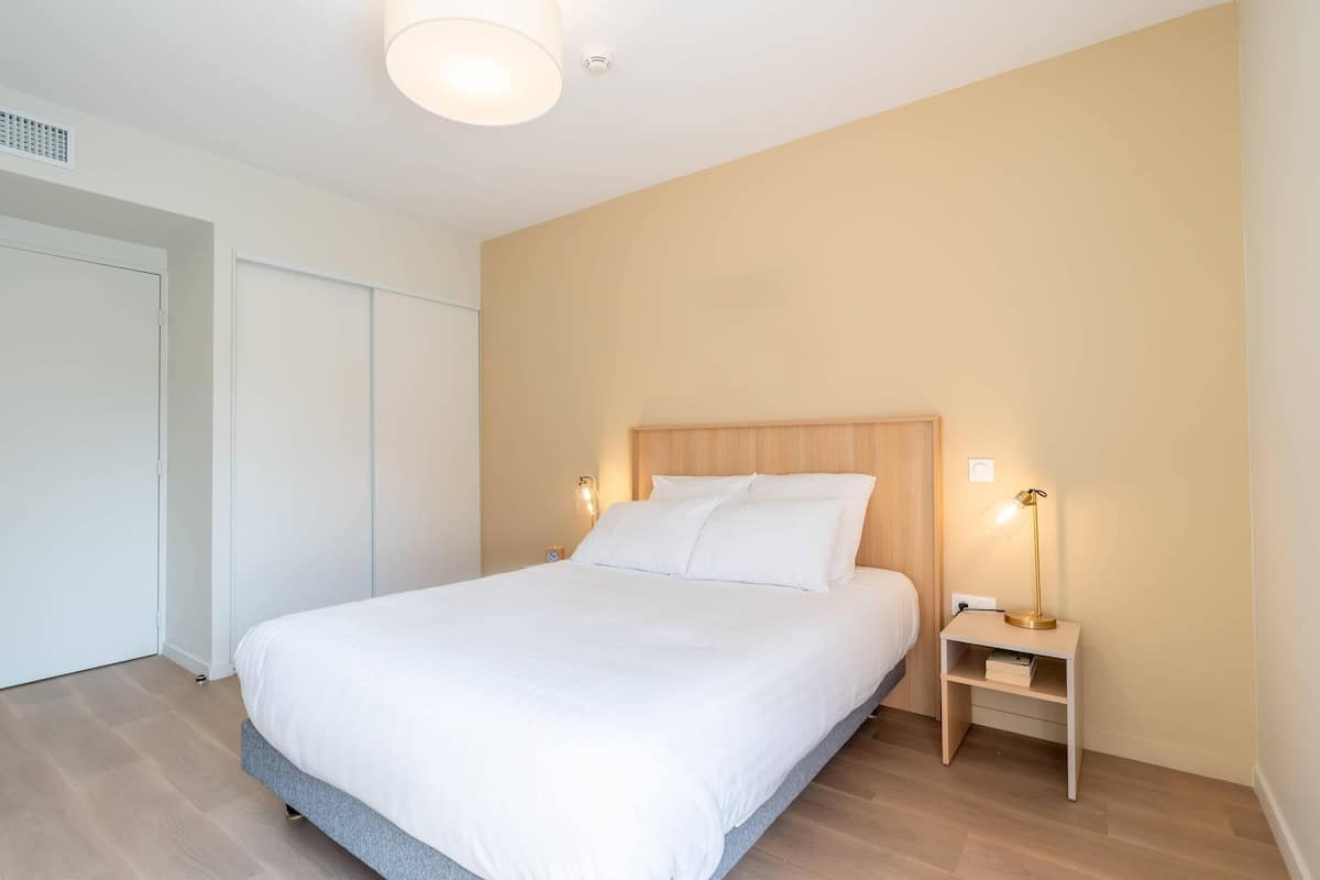 A bedroom with a bed, bedside lamps, a nightstand, and a door.