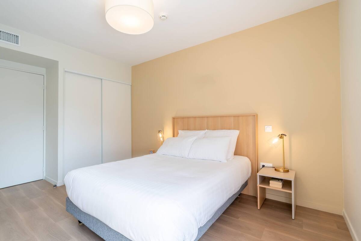 A bedroom with a bed, bedside lamps, a nightstand, and a door.
